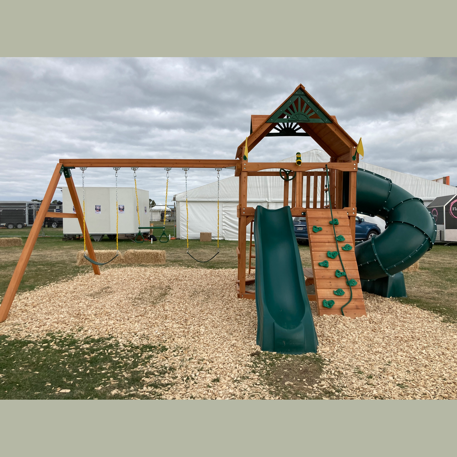 Wooden playground structure with slides and swings in an outdoor setting.