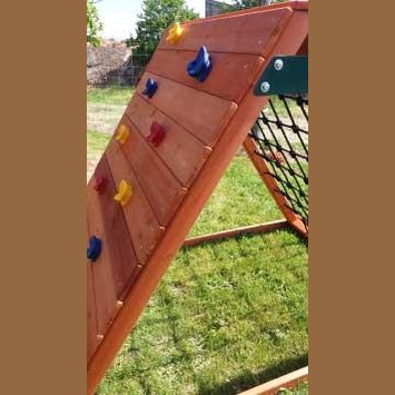 Children's wooden climbing wall with colorful rock holds on a grassy area
