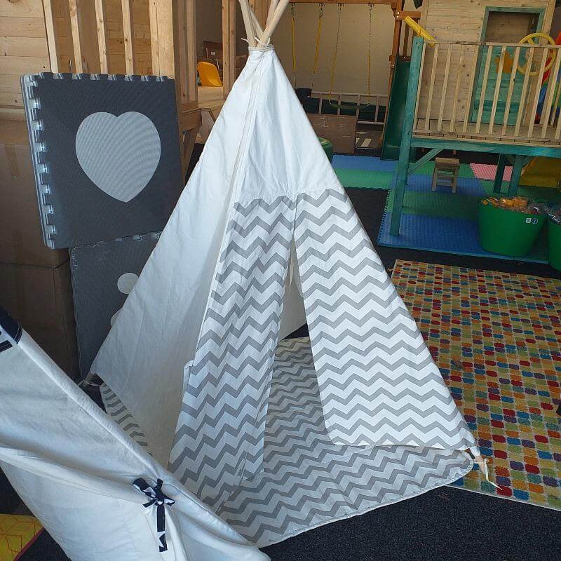 White and gray chevron-patterned teepee in a playroom with colorful mats and a wooden slide.