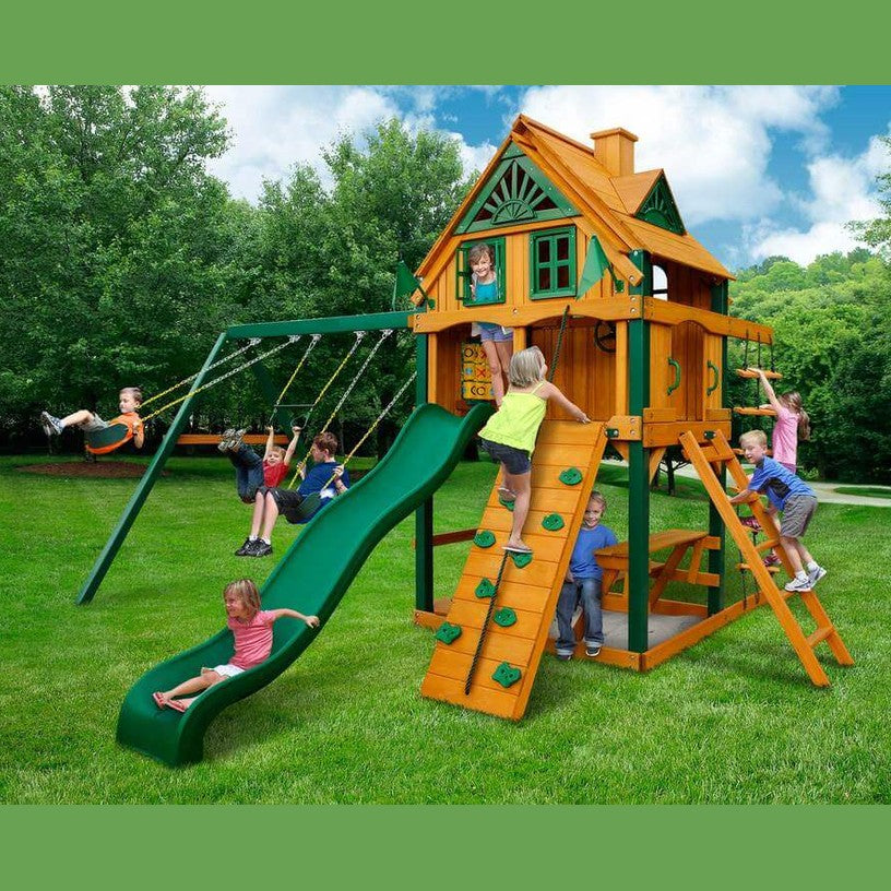 Children playing on a wooden playground set with a green slide and swings.
