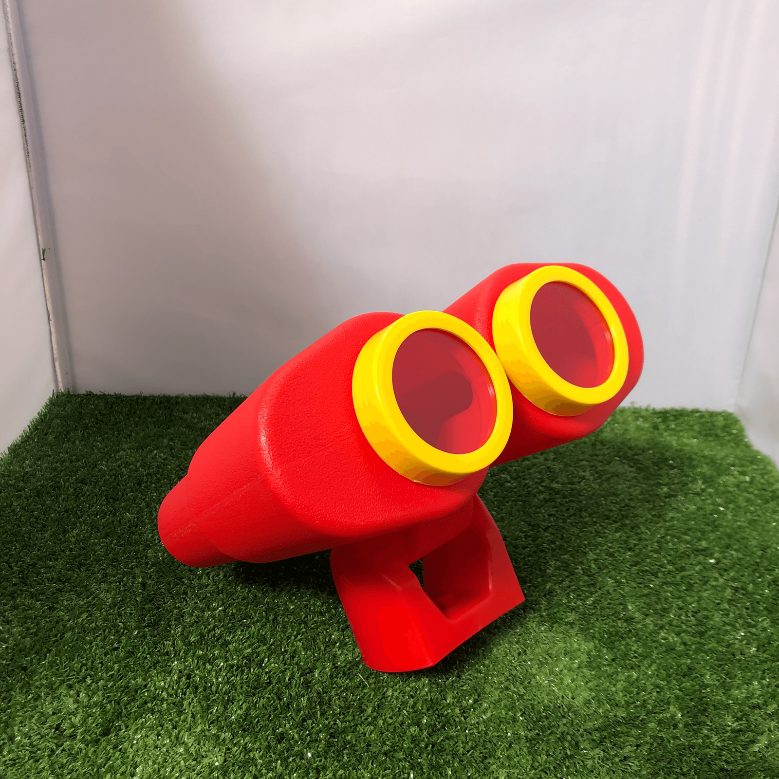 Red and yellow toy binoculars on a green grass-like surface