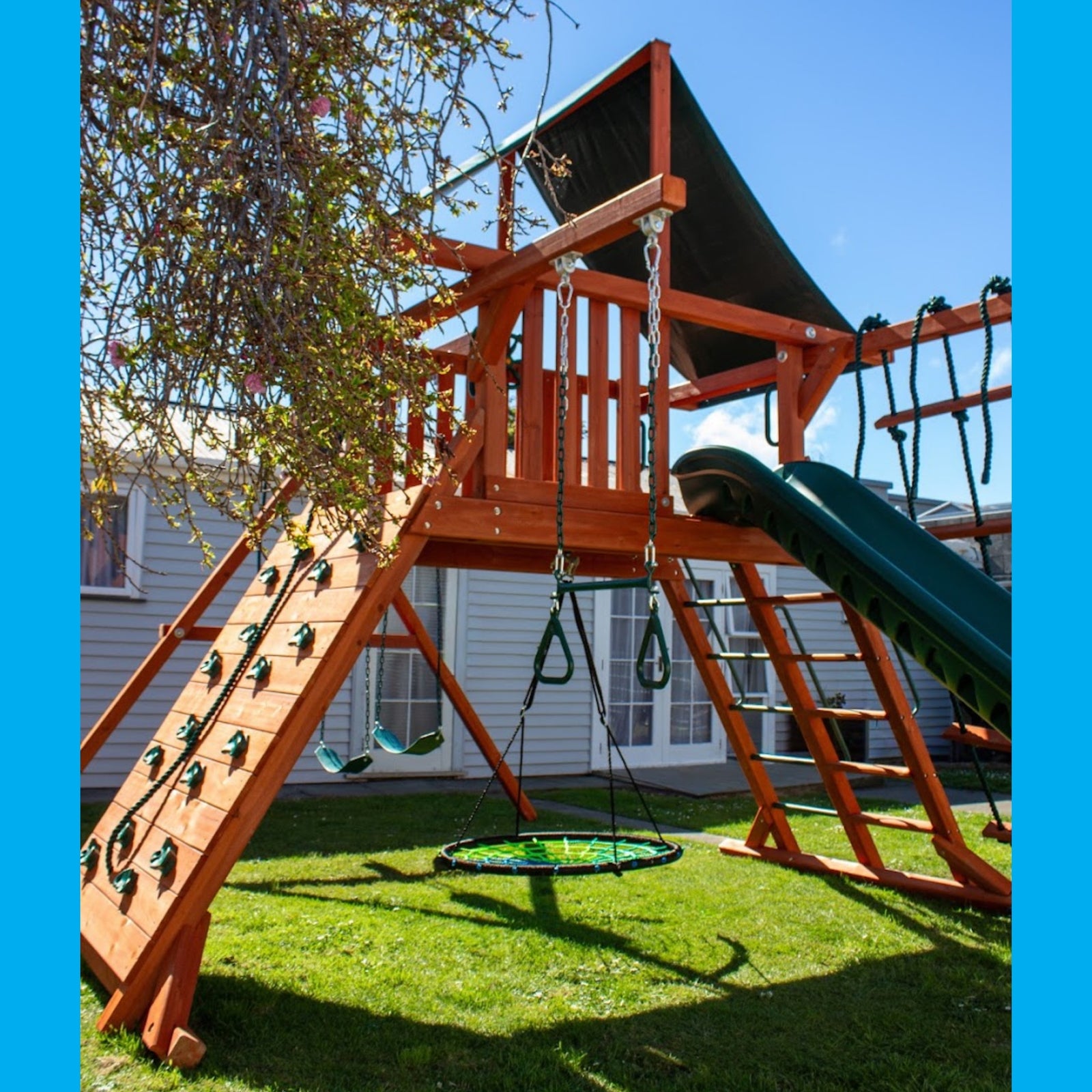 wooden cedar playground in NZ backyard with swings, slide, climbing rope and climbing wall