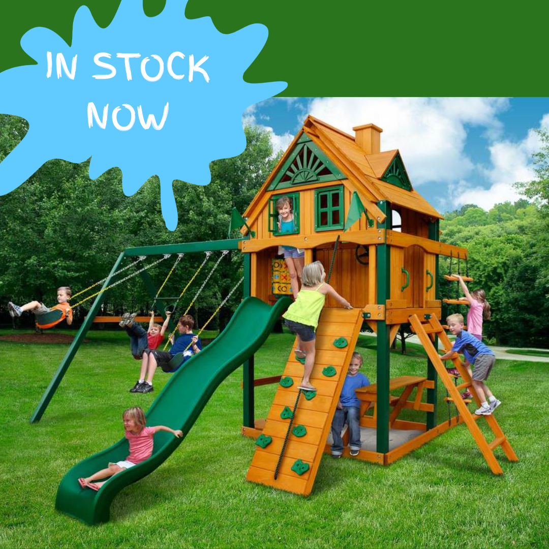 Children playing on a wooden playset with a green slide and swings, set against a clear blue sky.