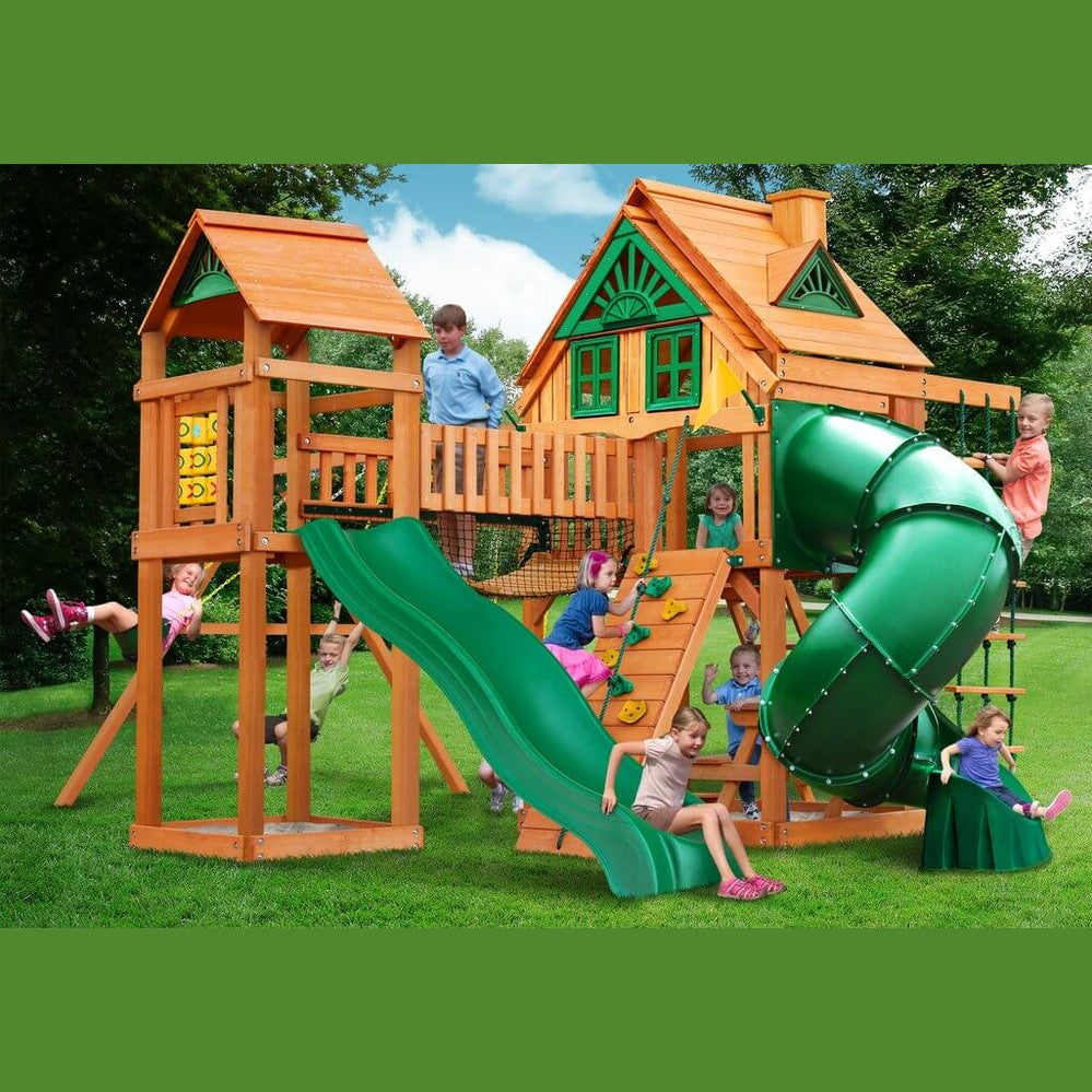 Children playing on a wooden playset with green slides in a backyard