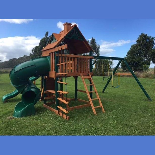 Children playing on a wooden playset with green slides in a backyard