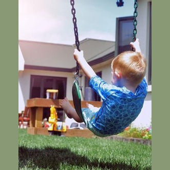 Child swinging on a swing set in a backyard with a house in the background