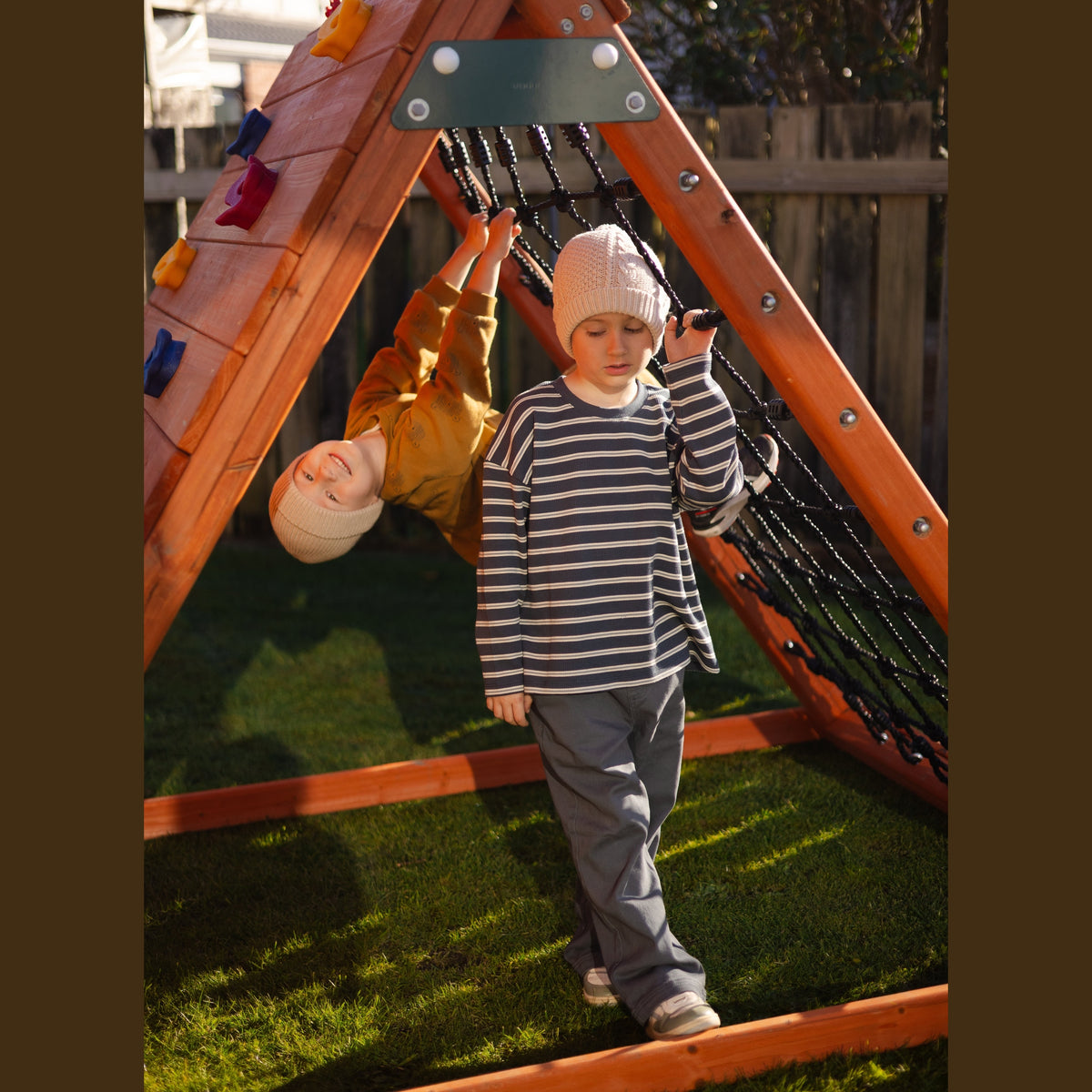 two children playing under the climbing frame with rock holds and scramble net