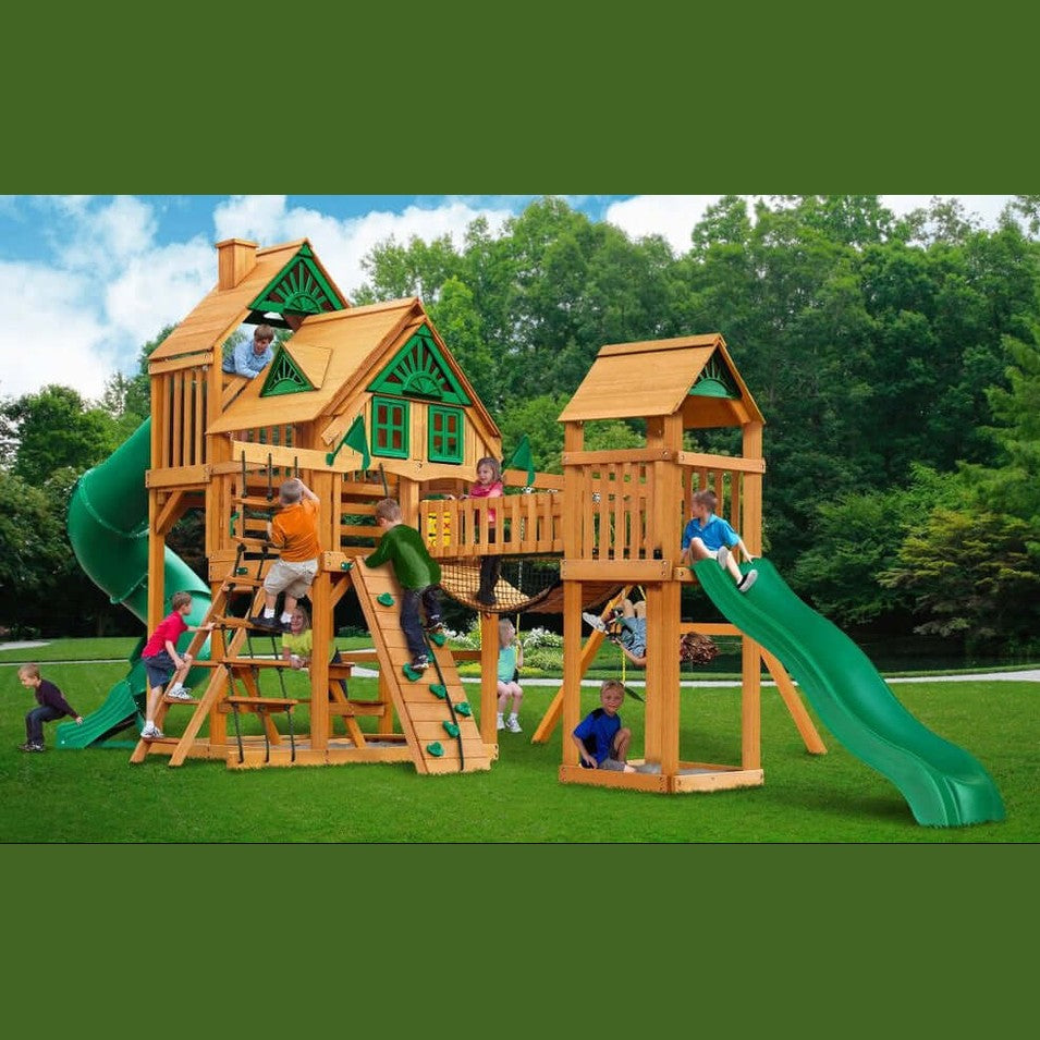 children playing on an outdoor wooden playground with lots of swings, 2 slides, rock wall, rope ladder and swingbridge 