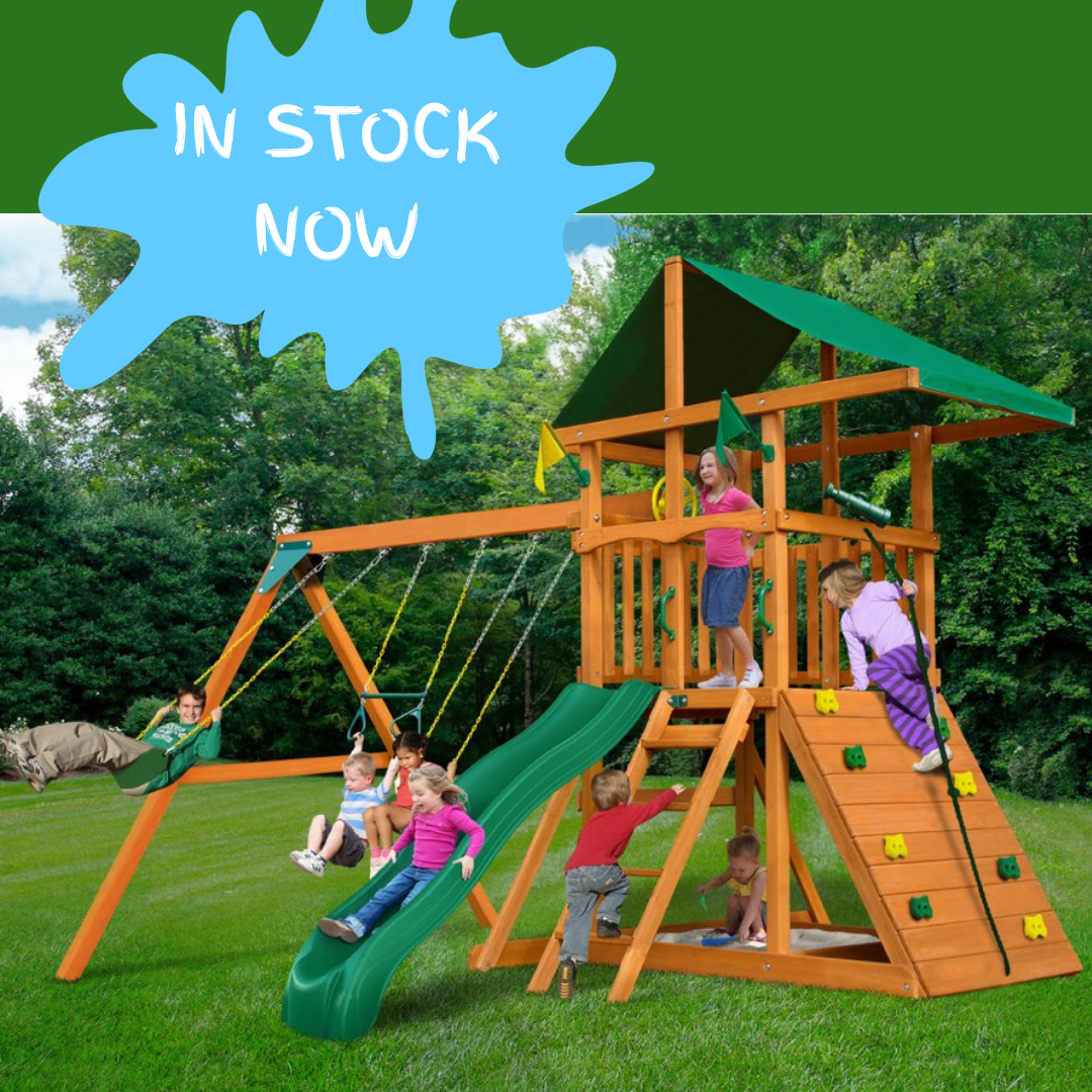 Children playing on a wooden playground set with a green slide and swings, surrounded by trees.