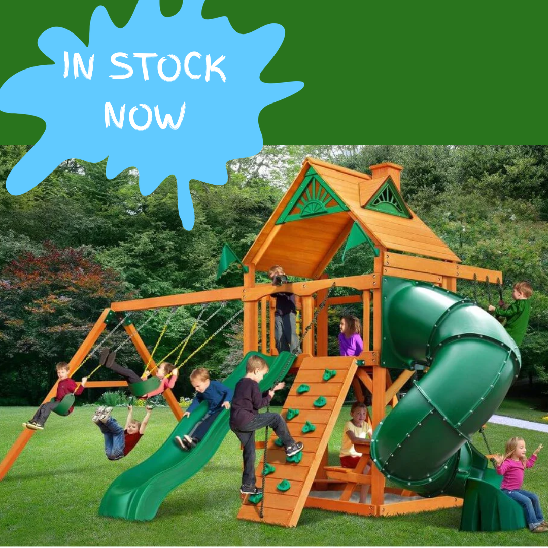 Children playing on a wooden playground set with a green slide, surrounded by trees.