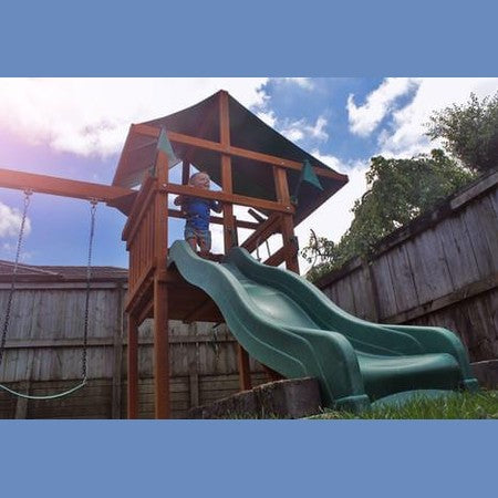 Child playing on a wooden playground set with a green slide in a backyard.