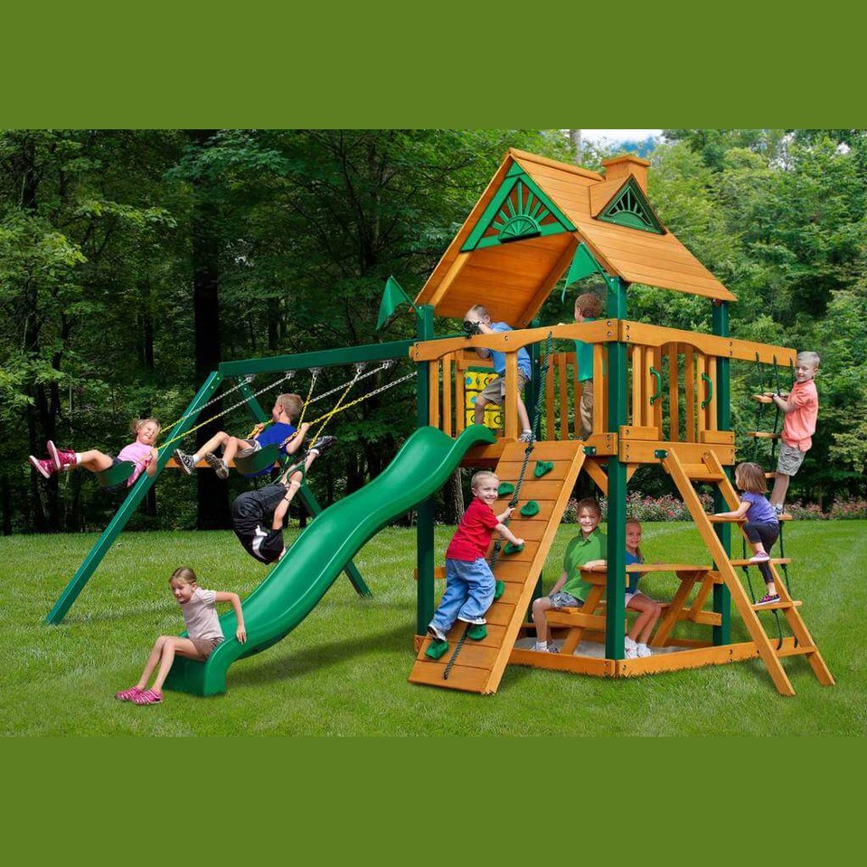 Children playing on a wooden playground set with green slide and swings in nz backyard