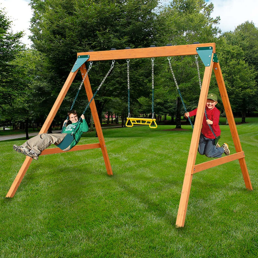 Two children playing on a wooden swing set in a park with green grass and trees.