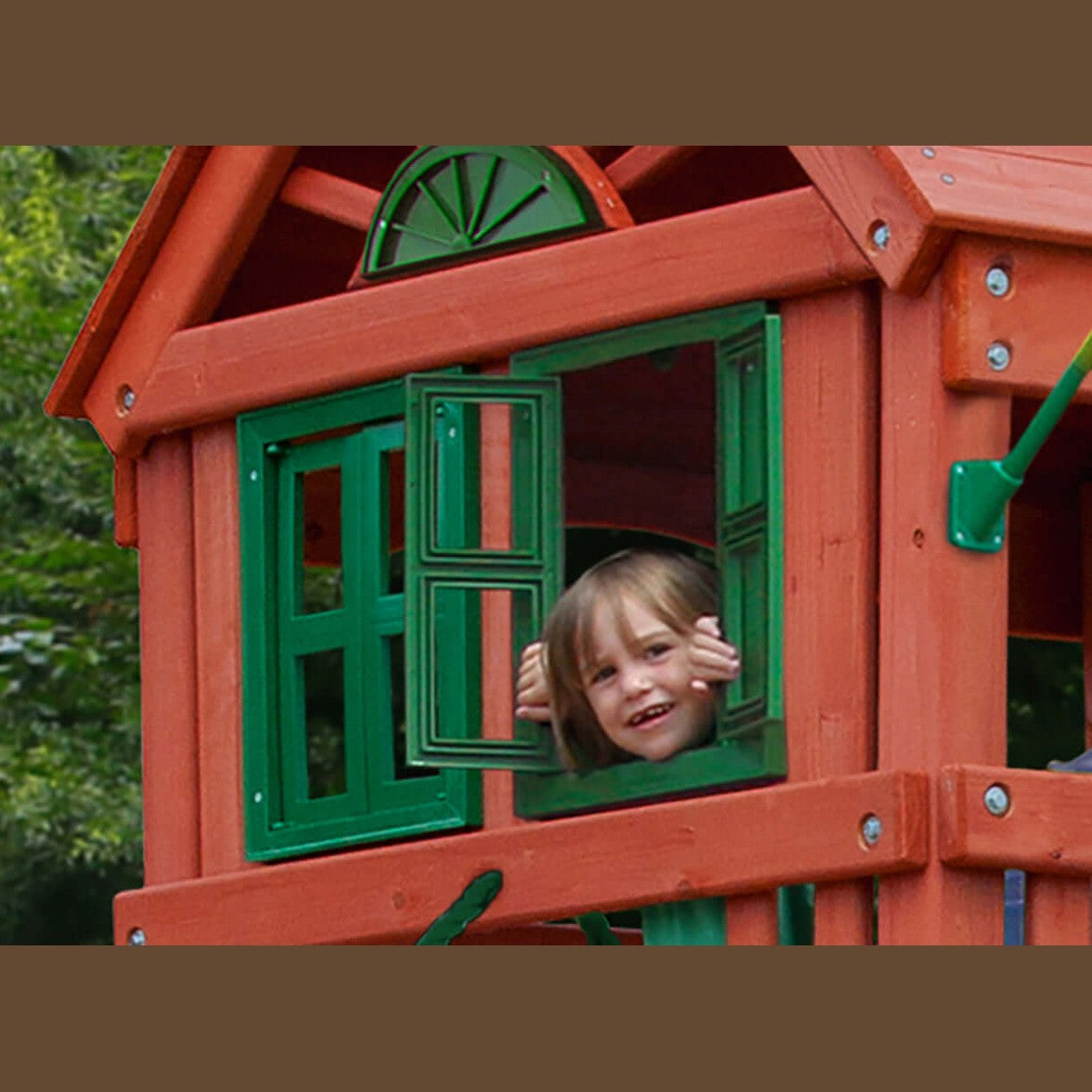 Child peeking out from a window of a red playhouse with green shutters.